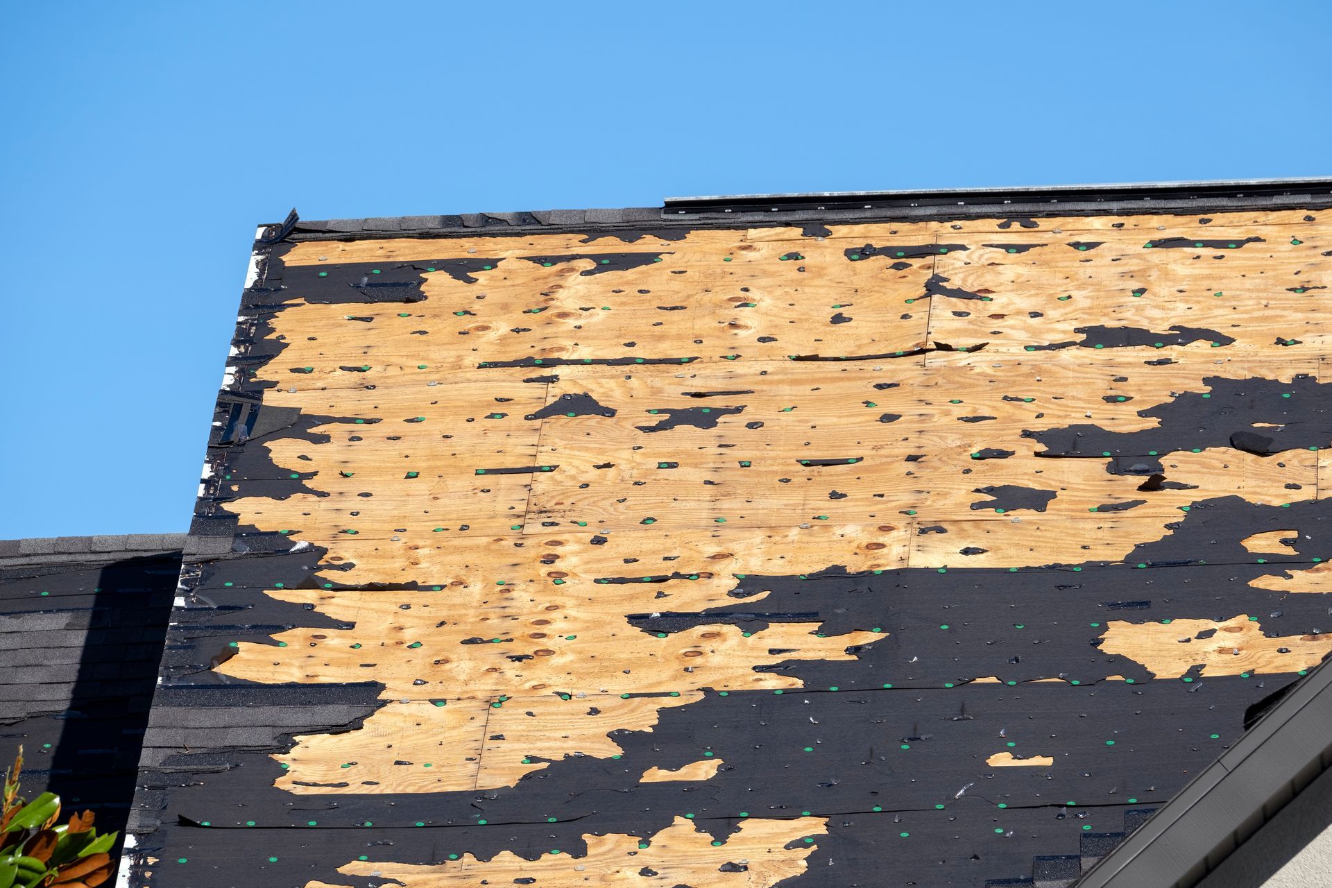 Partially shingled roof with exposed wood and blue sky background.