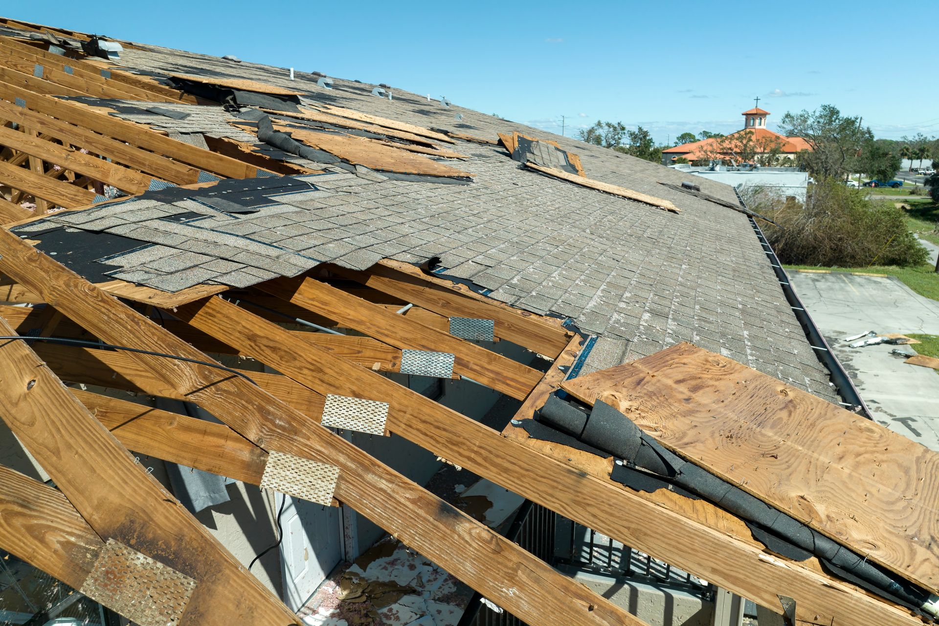 Damaged roof: wooden beams exposed, roofing material torn off, sky overhead.