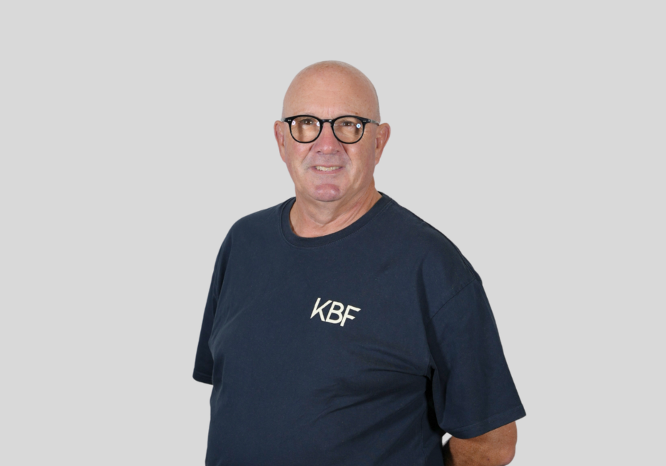 A bald man wearing glasses and a blue shirt that says kbf