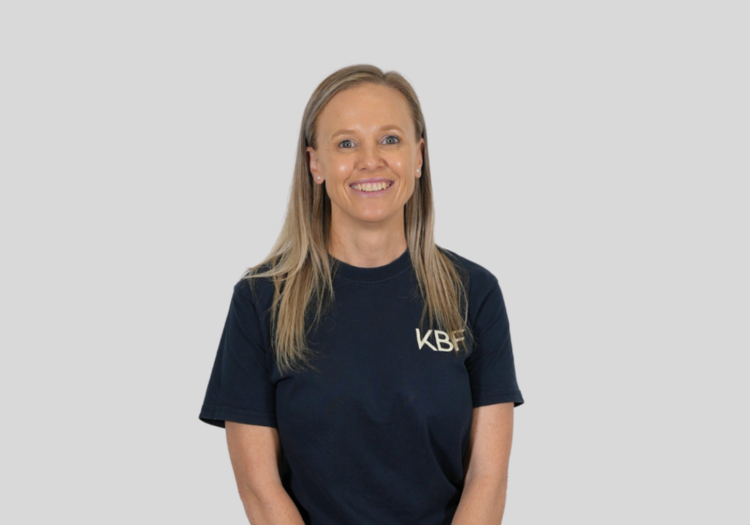 A woman wearing a blue t-shirt with the word kb on it is smiling.
