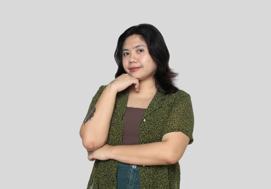 A woman in a green shirt is standing with her arms crossed and her hand on her chin.