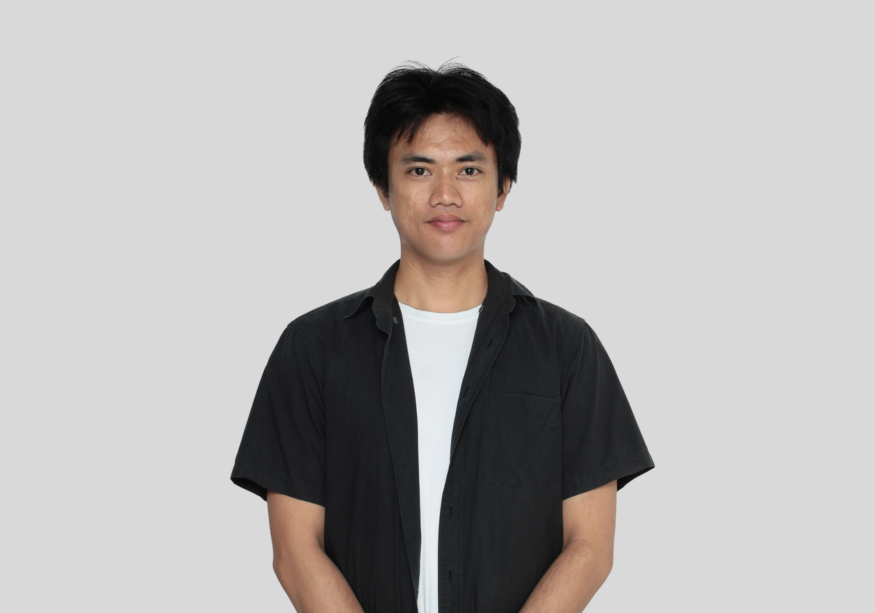 A man in a black shirt and white t-shirt is standing in front of a white background.