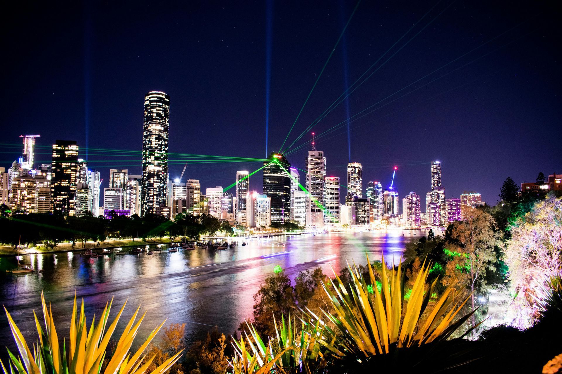 Night skyline over a river at dusk, with colorful city lights reflecting on the water.