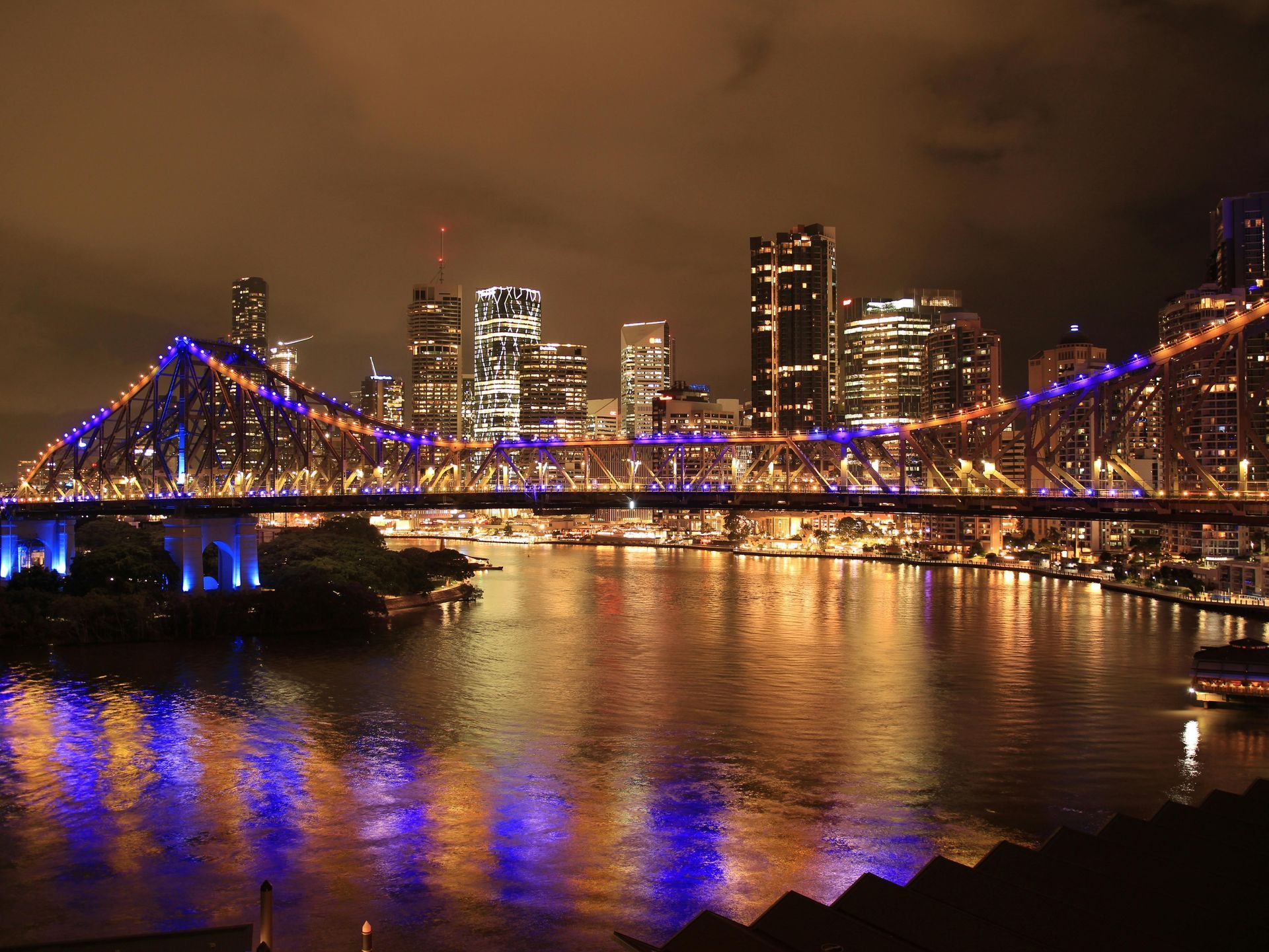 Night city skyline with a lit bridge reflecting blue and gold lights on the water