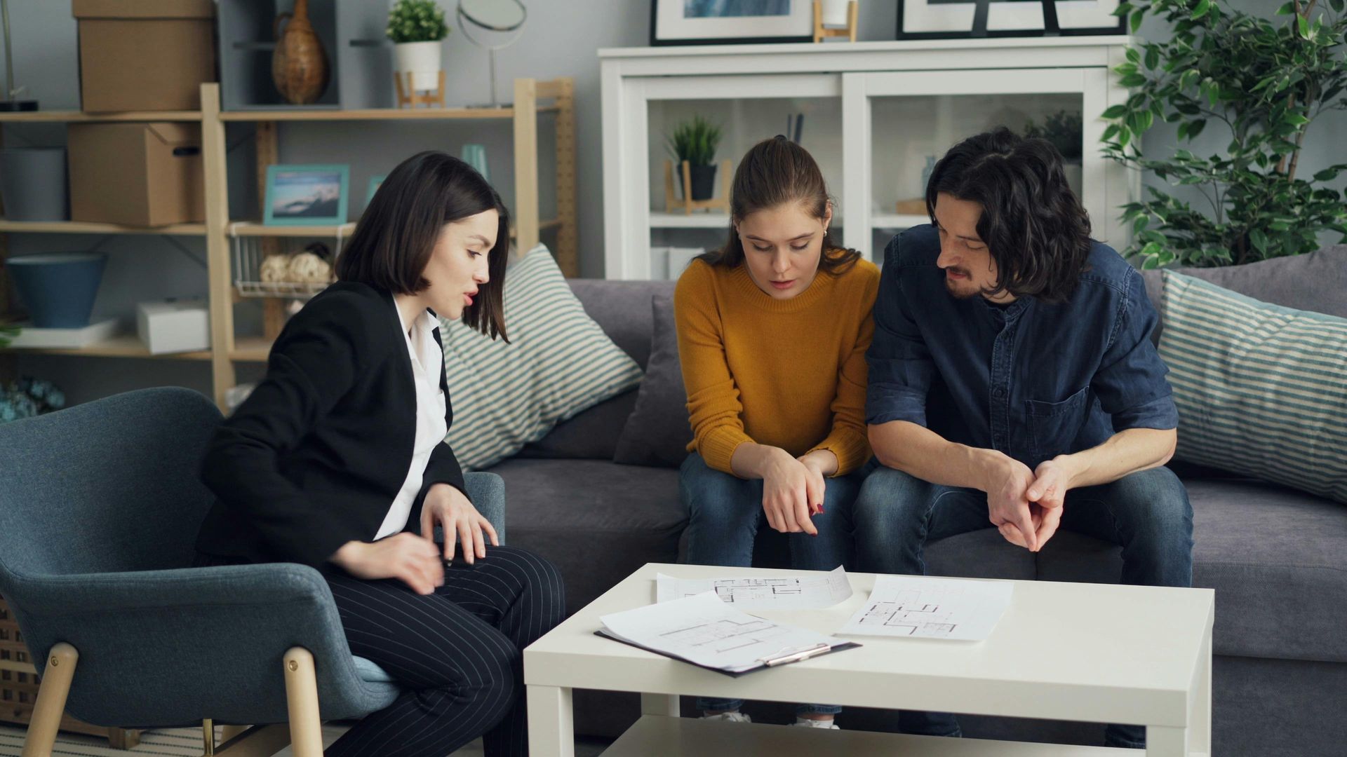 Three people on a couch discussing papers around a coffee table in a living room