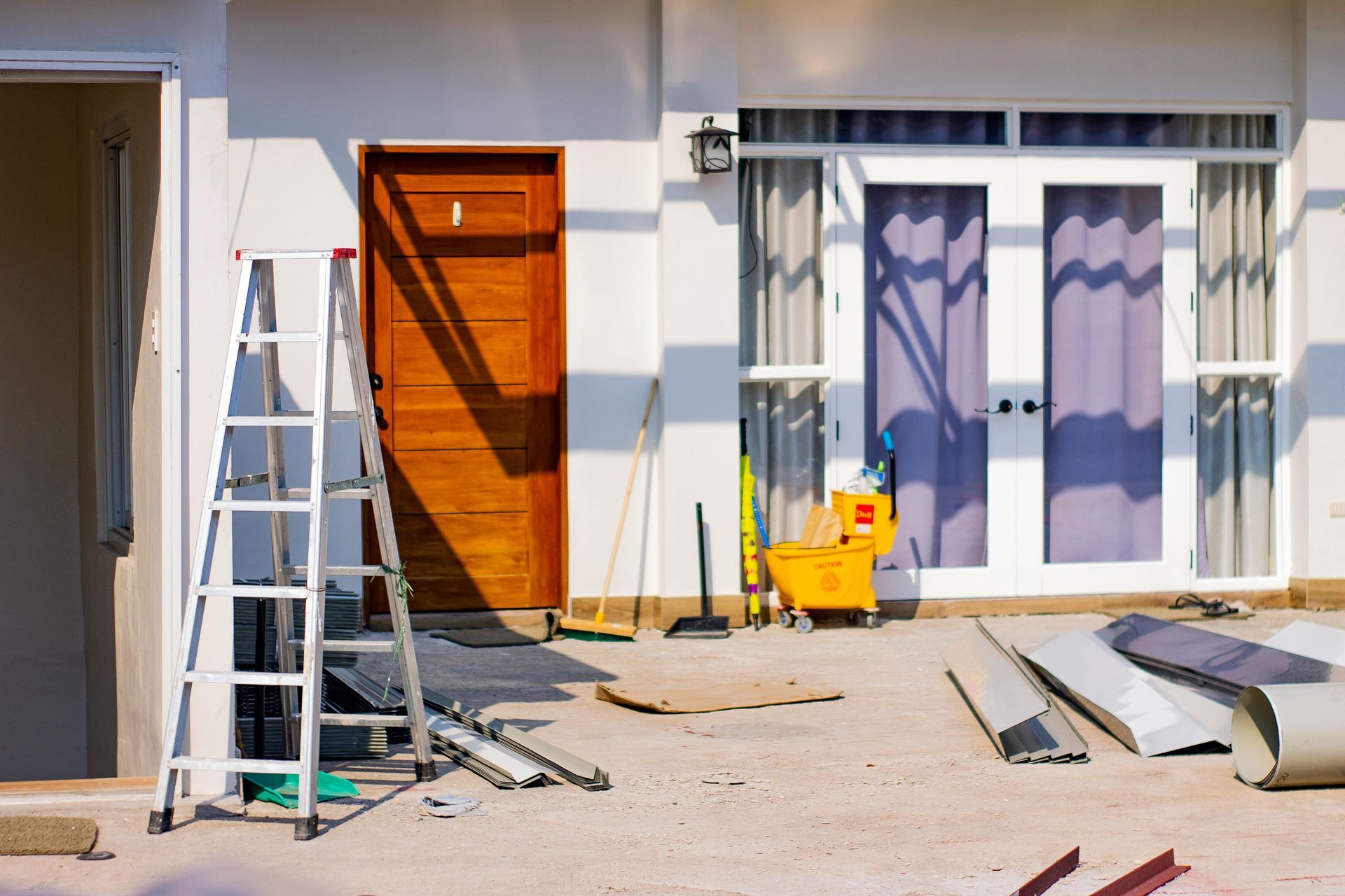 Front of a house under renovation with a ladder, tools, and construction materials on the patio.