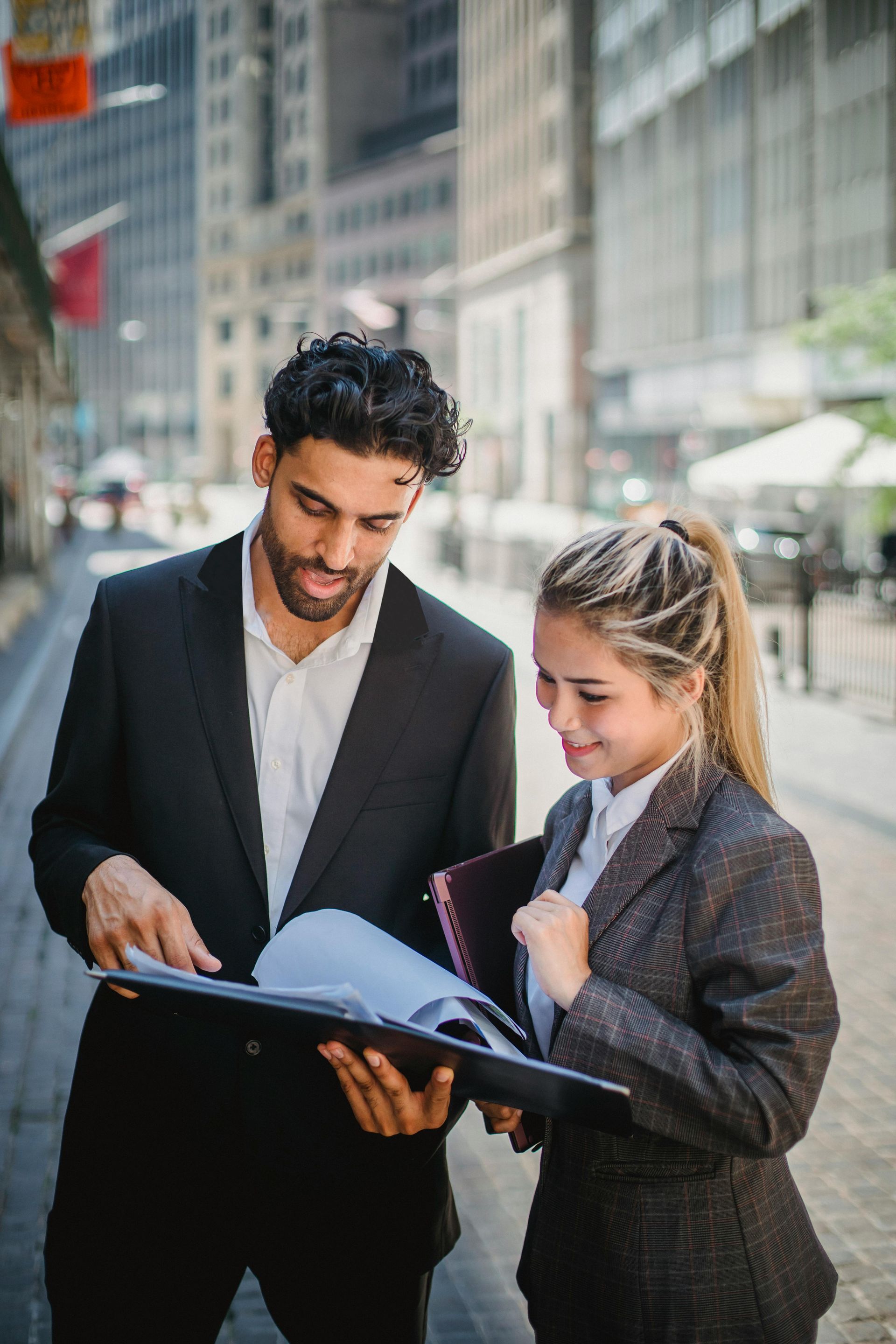 Two professionals reviewing documents on a sidewalk in a city setting