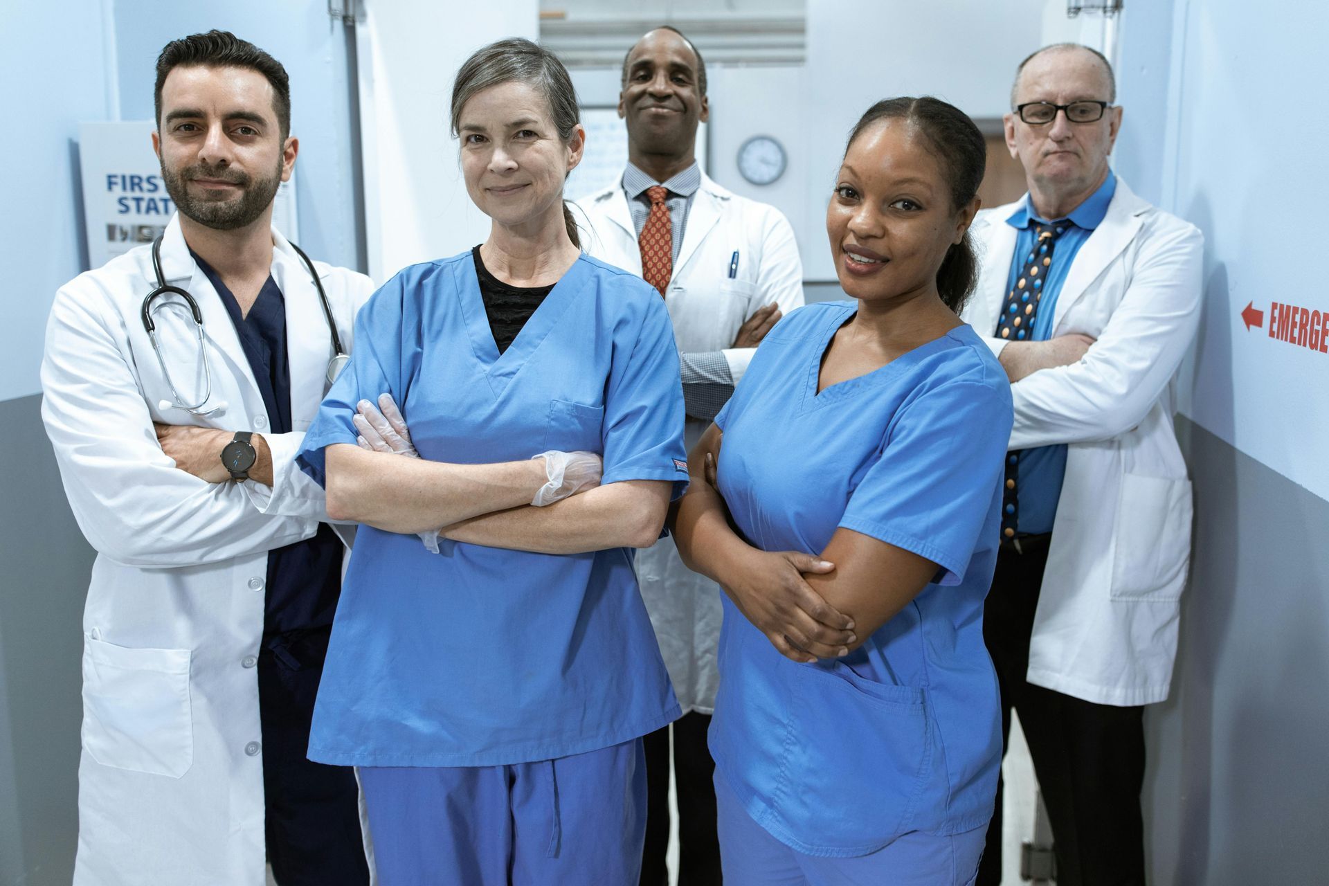 Medical team in blue scrubs and white coats standing together in a hospital hallway