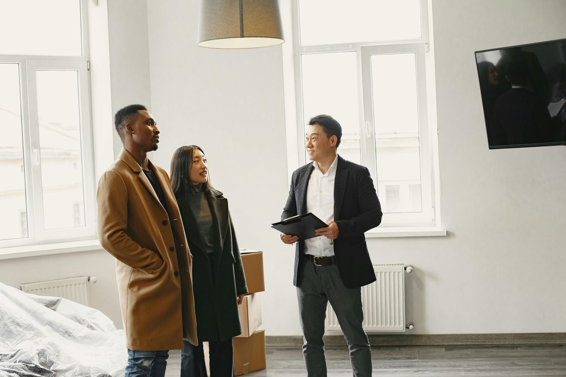 Three people talking in a bright, modern room with large windows and a wall-mounted TV.