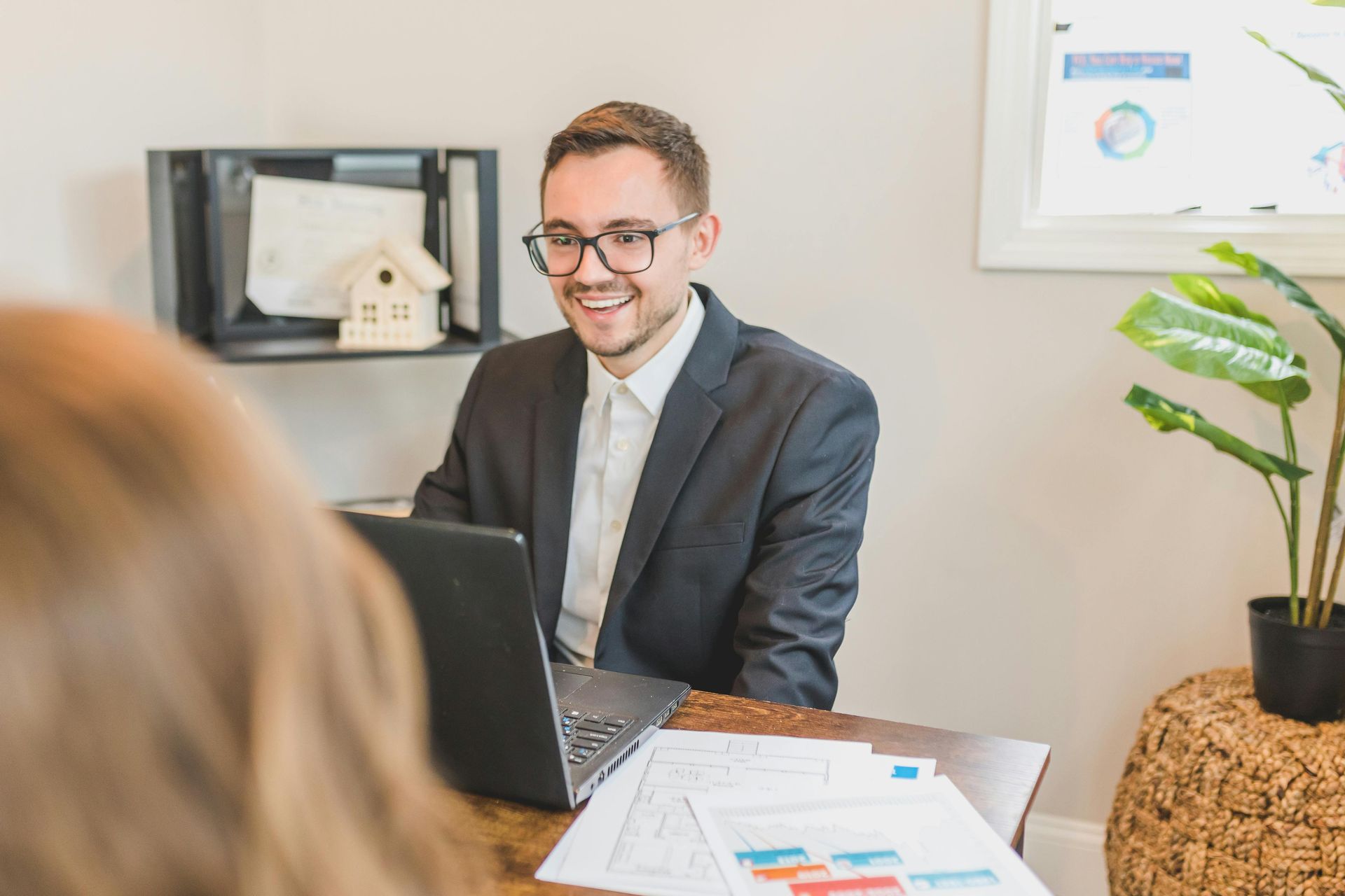 Smiling man in suit meeting with a client across a laptop in a bright office