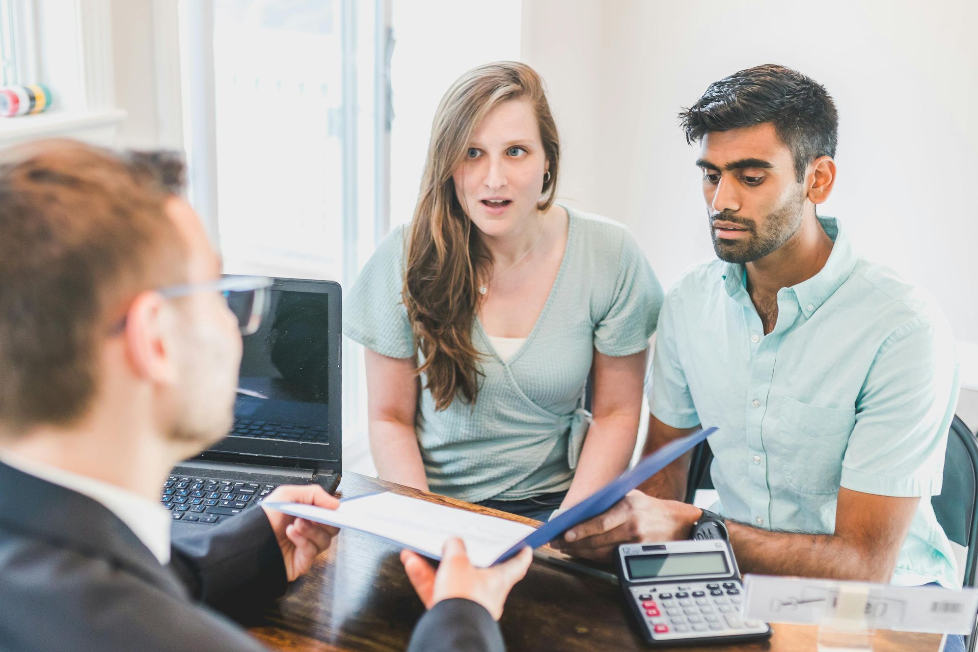 Three people in a meeting, discussing documents across a desk in an office.