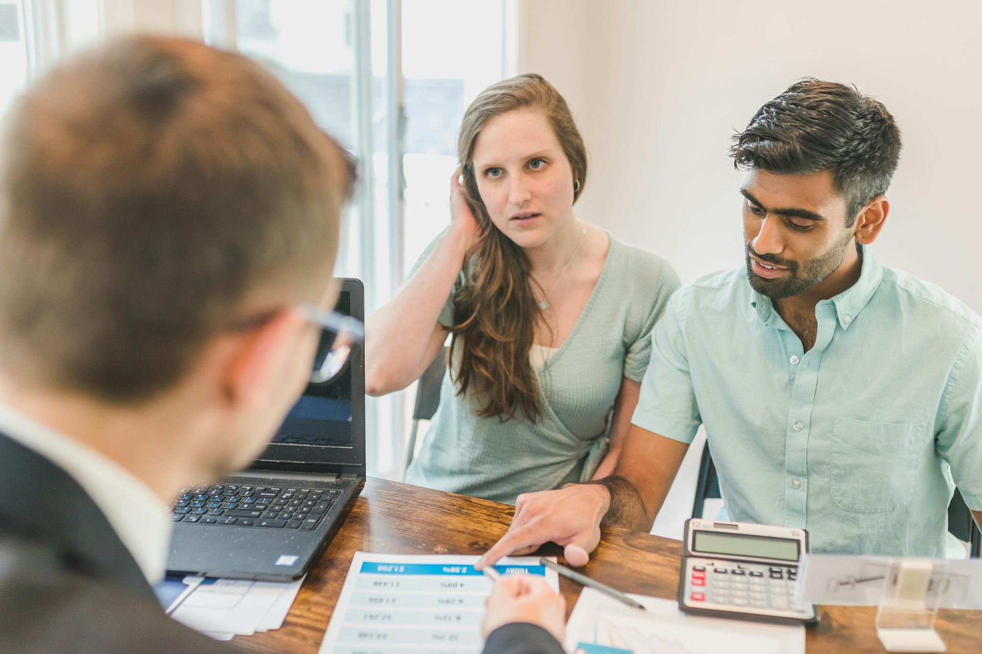 Business meeting with two clients at a desk, discussing documents across from a blurred person in the foreground