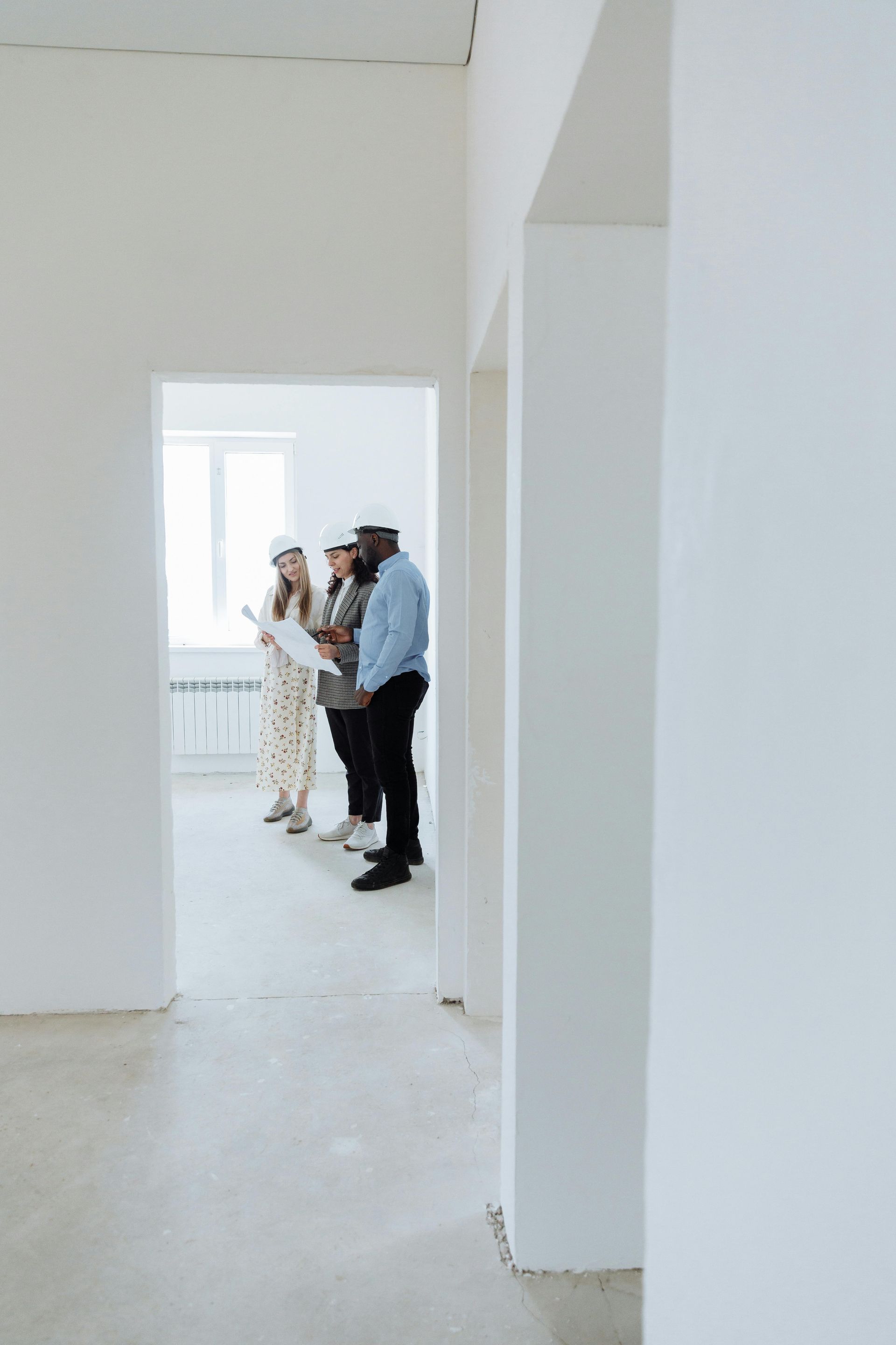 Three people wearing hard hats are talking inside an empty room.