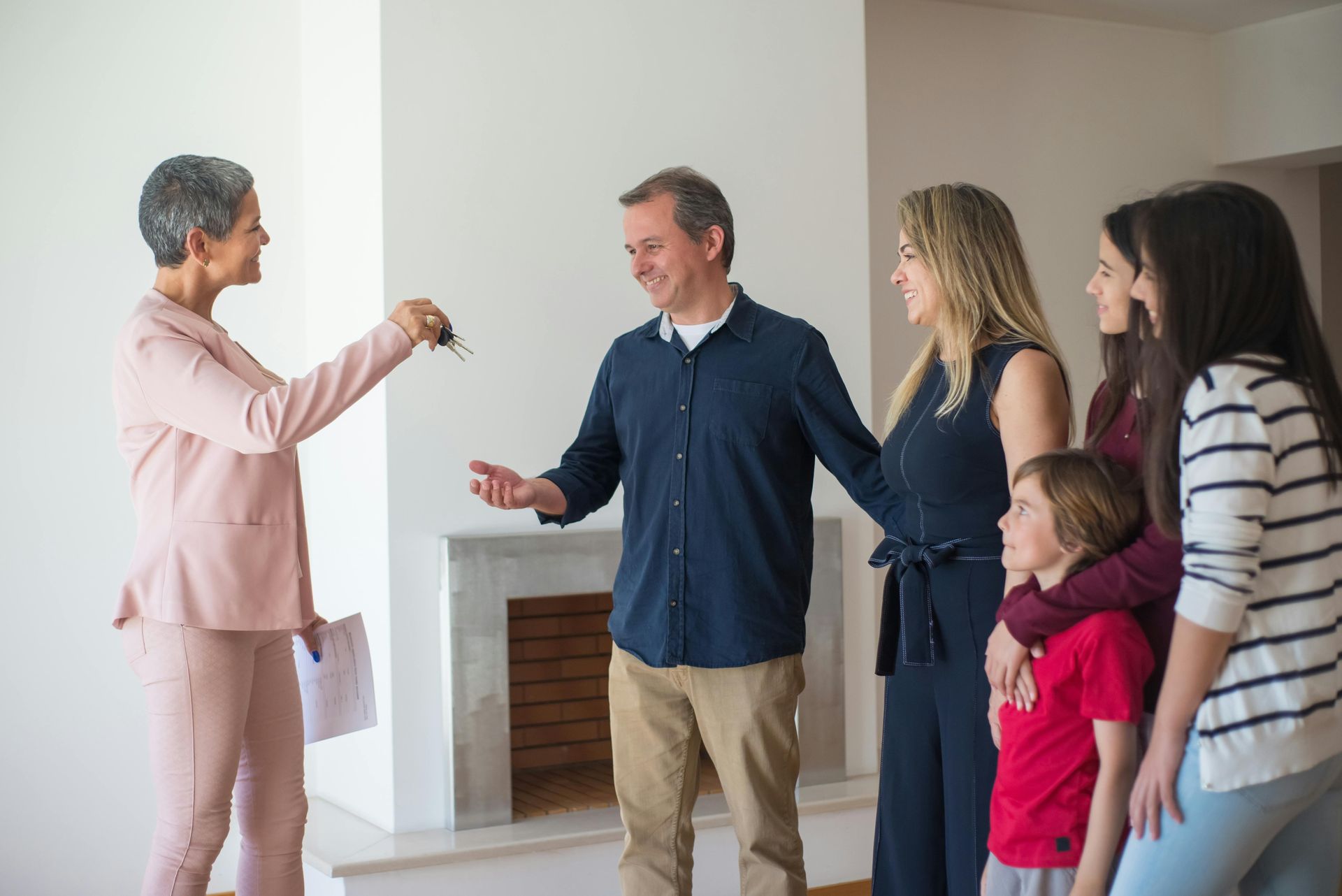 Four people greet a woman in a bright, empty room with open hands and smiles.