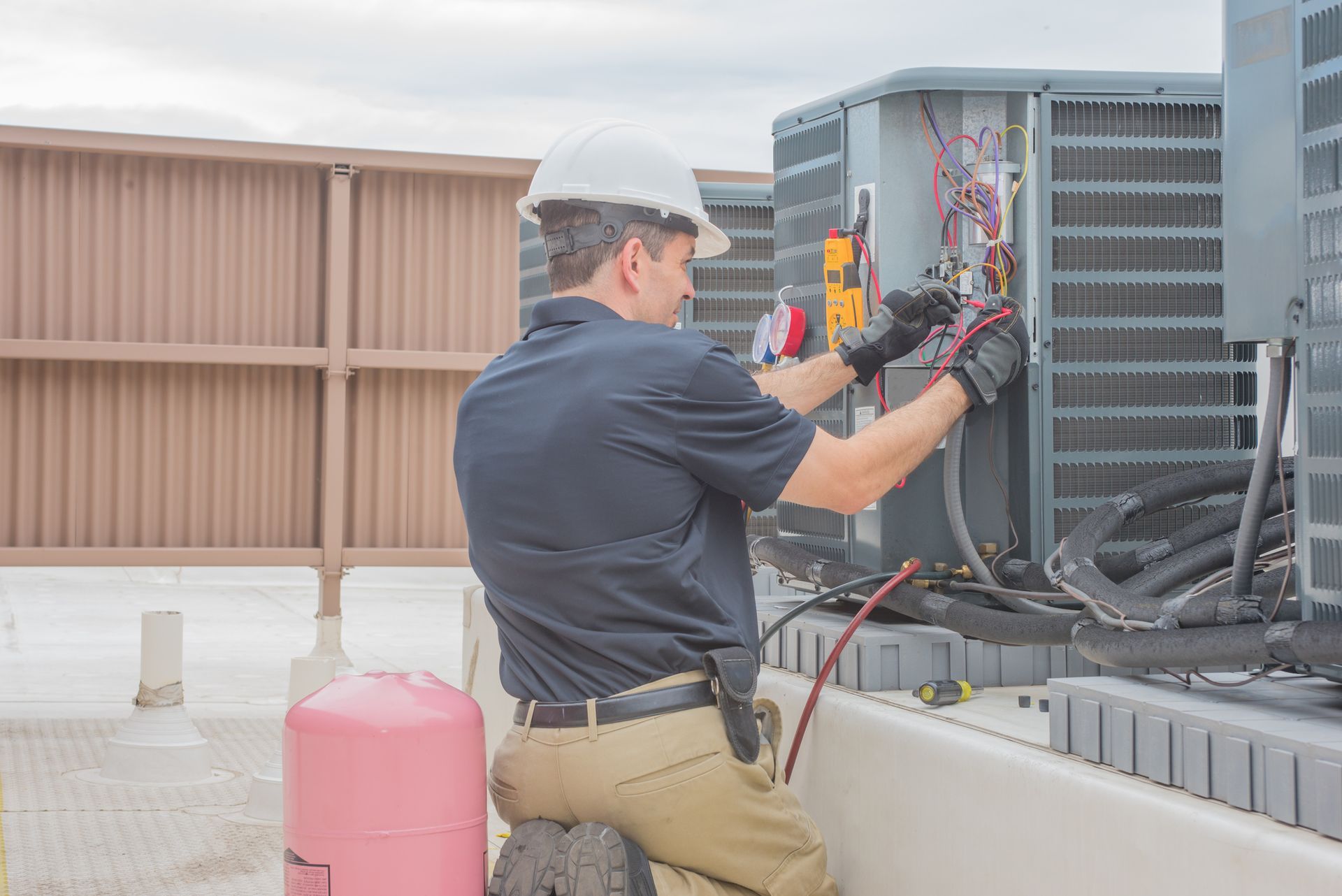 Male HVAC tech kneeling in front of a condenser unit, on a rooftop.