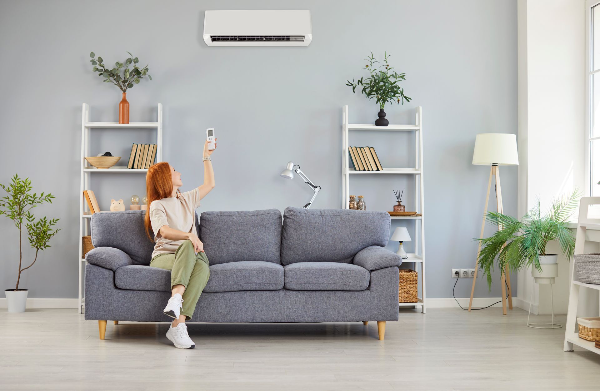 Smiling woman uses a remote control to turn on the air conditioner.