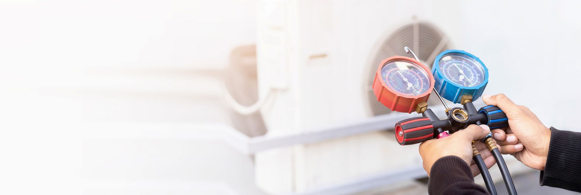 HVAC technician using manifold gauge to check air conditioner refrigerant pressure outdoors.