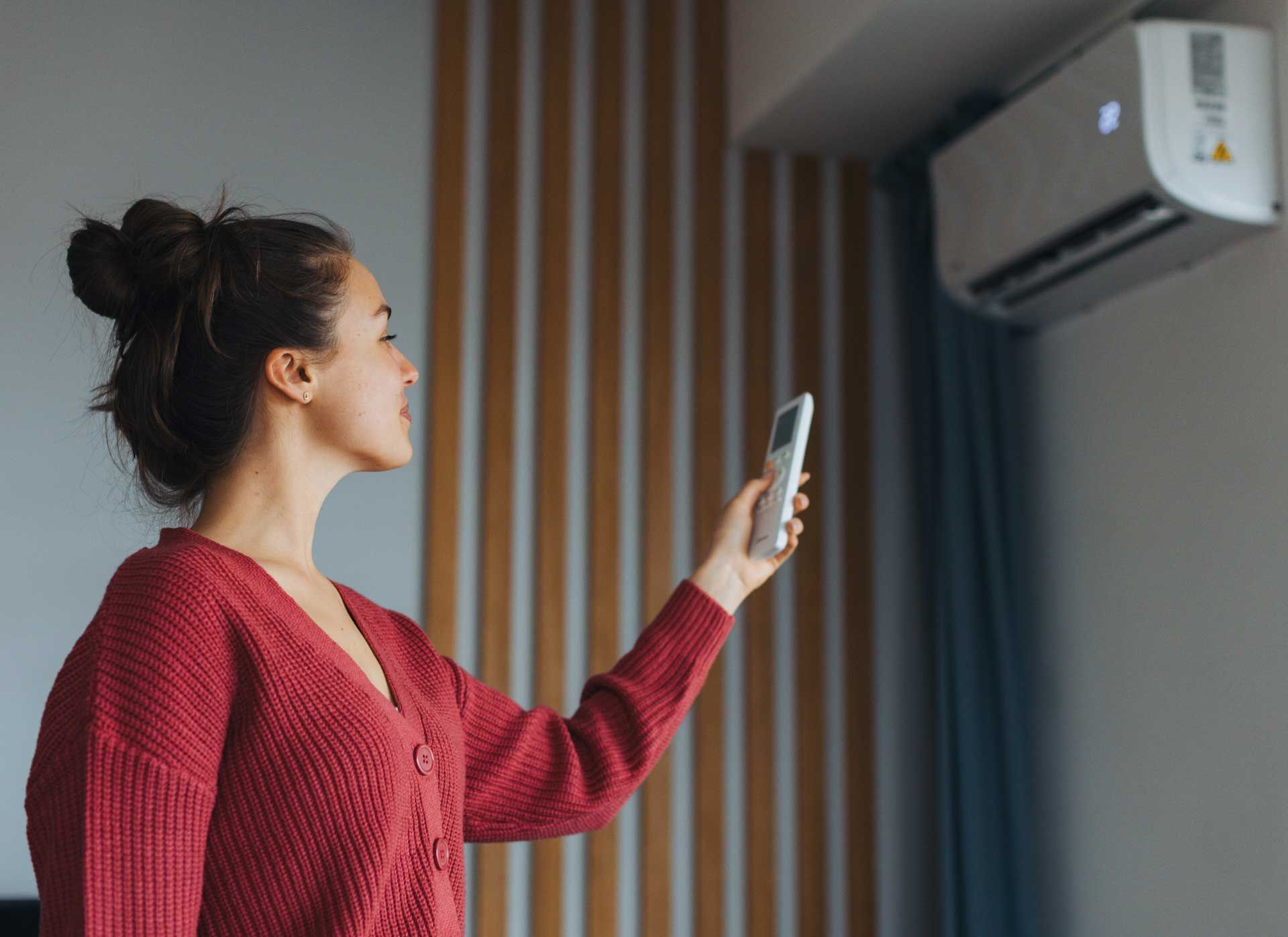 Woman adjusting the temperature of an air conditioner, holding a remote controller.