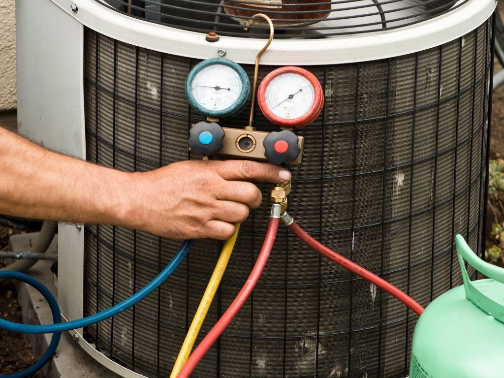 A man is working on an air conditioner with a hose attached to it.