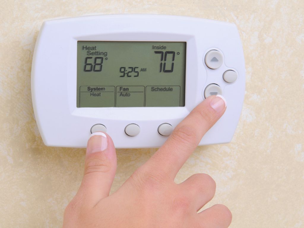 A person is pressing a button on a thermostat that is set to 70 degrees