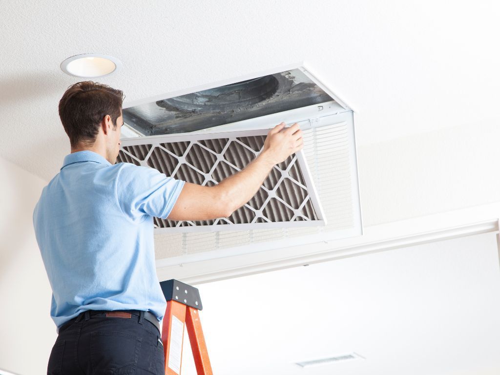 A man is standing on a ladder cleaning an air vent.