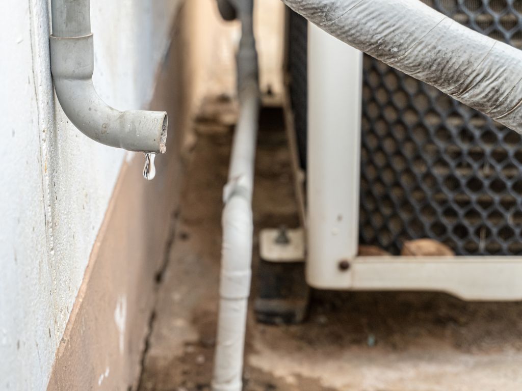 A close up of a pipe with water dripping from it next to an air conditioner.