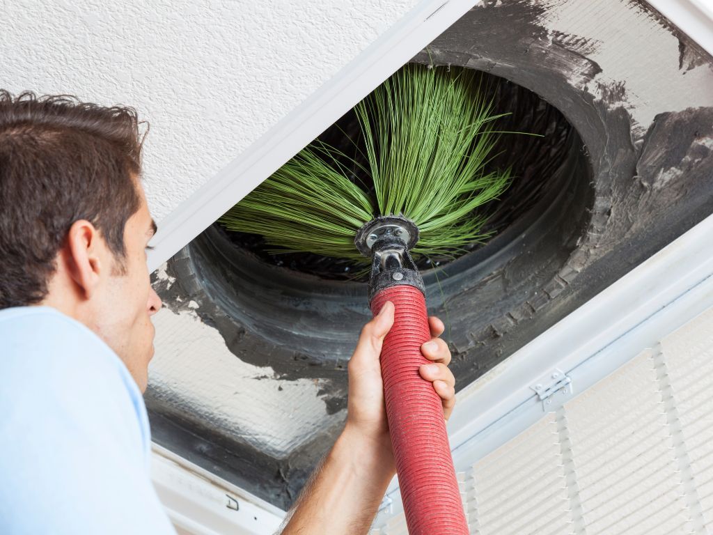 A man is cleaning an air vent with a brush.