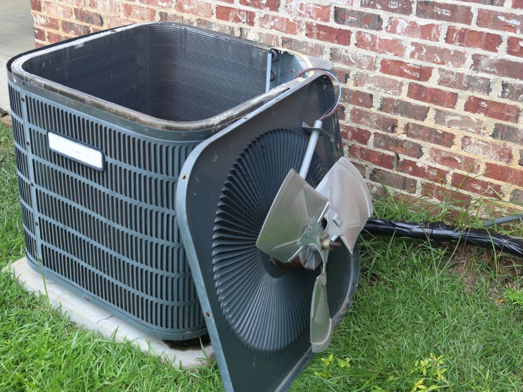 A broken air conditioner is sitting in the grass in front of a brick building.