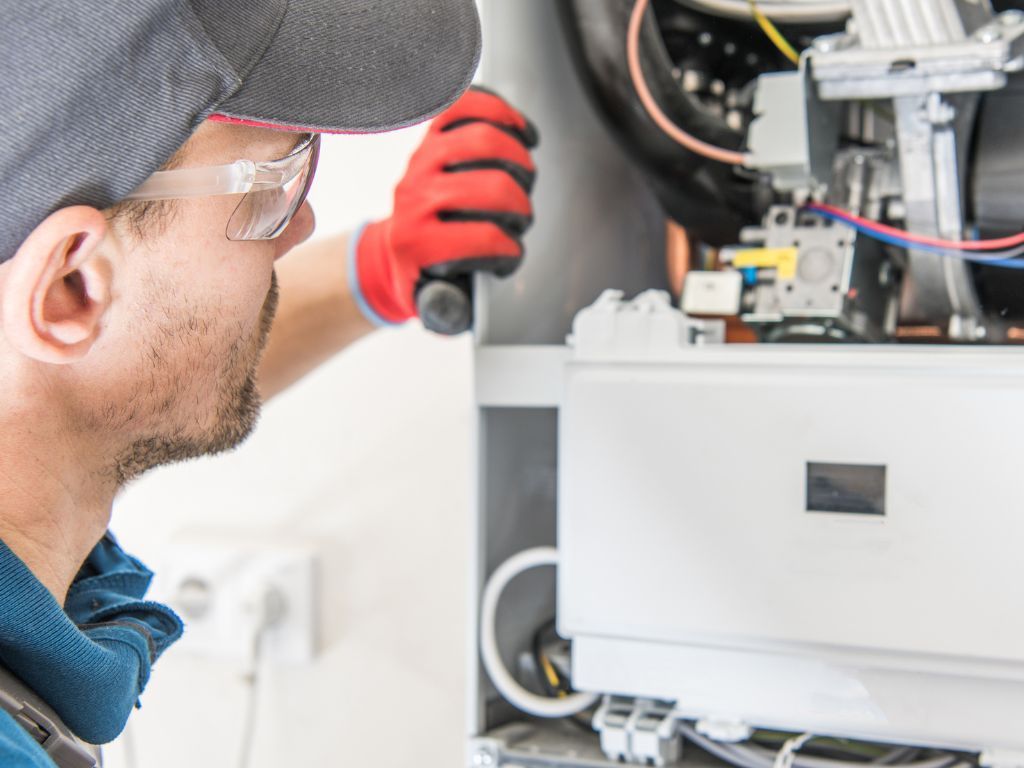 A man wearing a hat and gloves is working on a boiler.