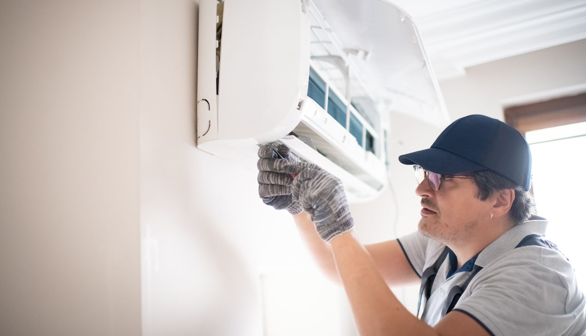 A technician wearing glasses performs air conditioning repair as part of a professional AC service.