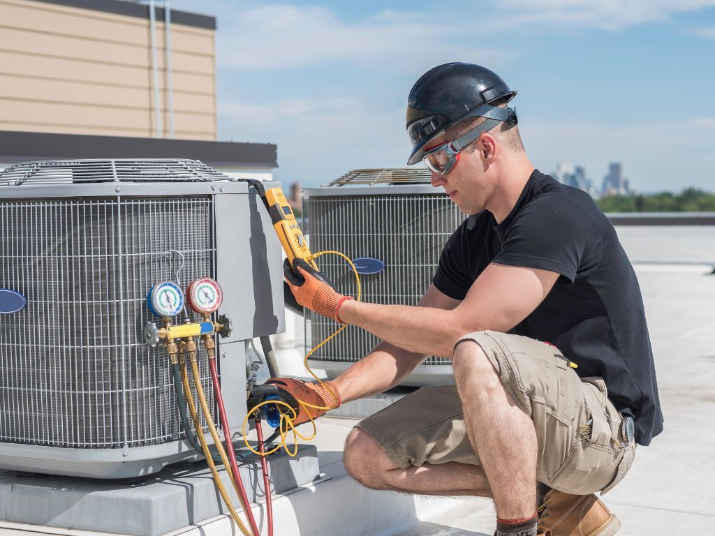 A man is working on an air conditioner on the roof of a building.