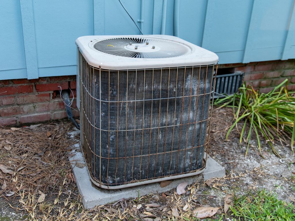 A dirty air conditioner is sitting outside of a house.