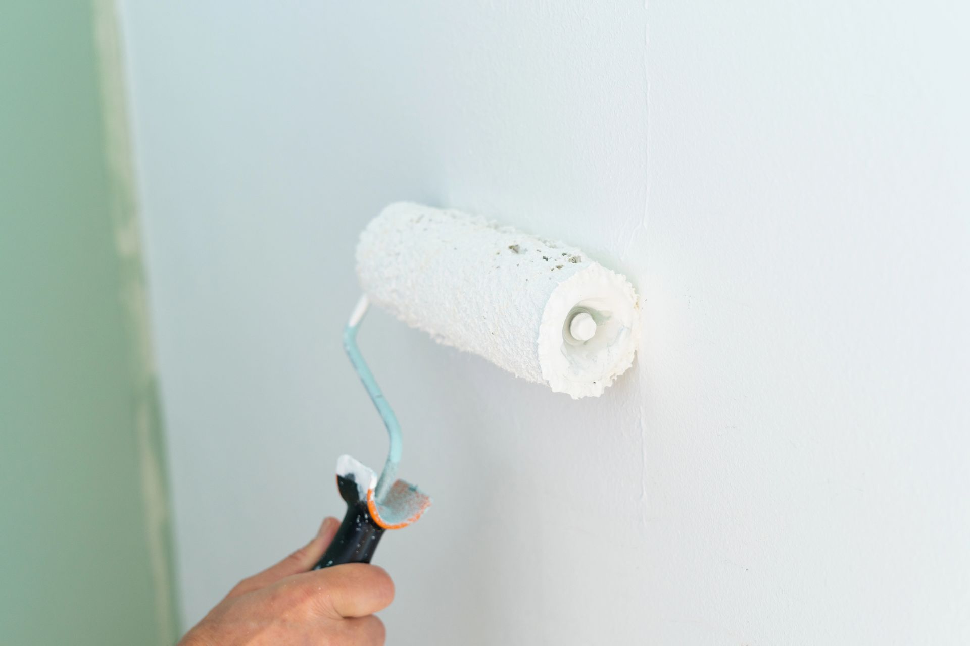 Persona che usa un rullo per applicare la vernice bianca su una parete.