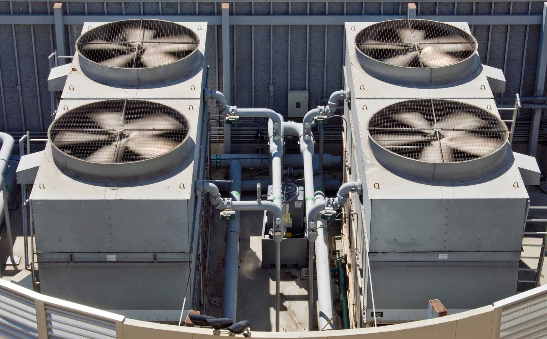 Four large rooftop HVAC units with visible fans and connecting pipes on a building roof