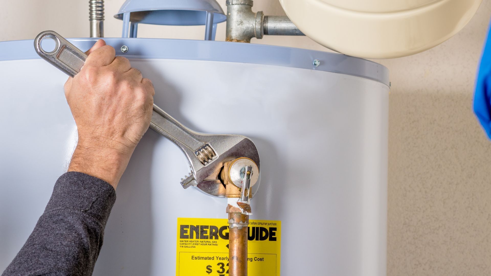 Person using a wrench to tighten a bolt on a gray tank with an energy guide label.