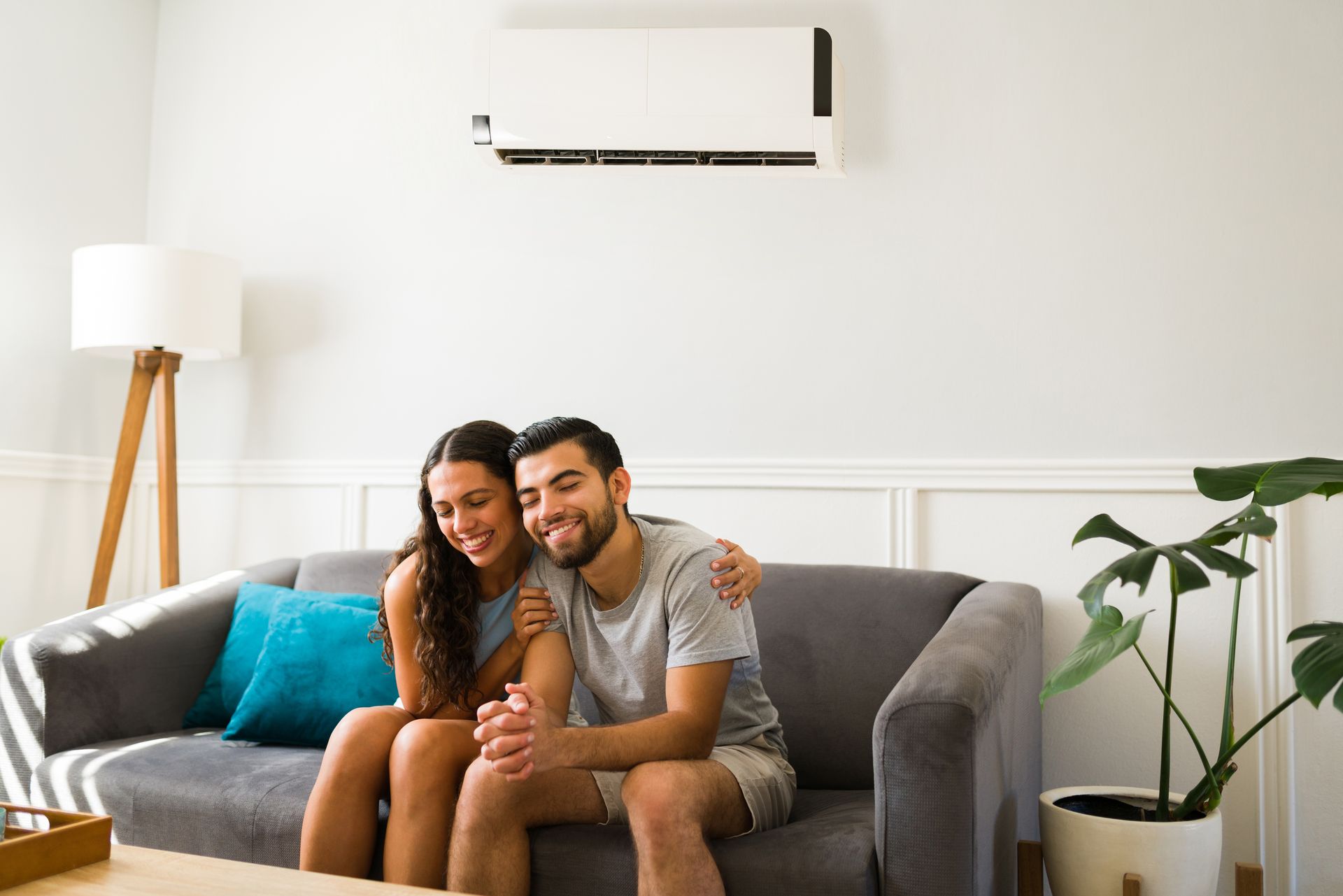 Couple smiling on gray couch under air conditioner. Bright, modern living room.