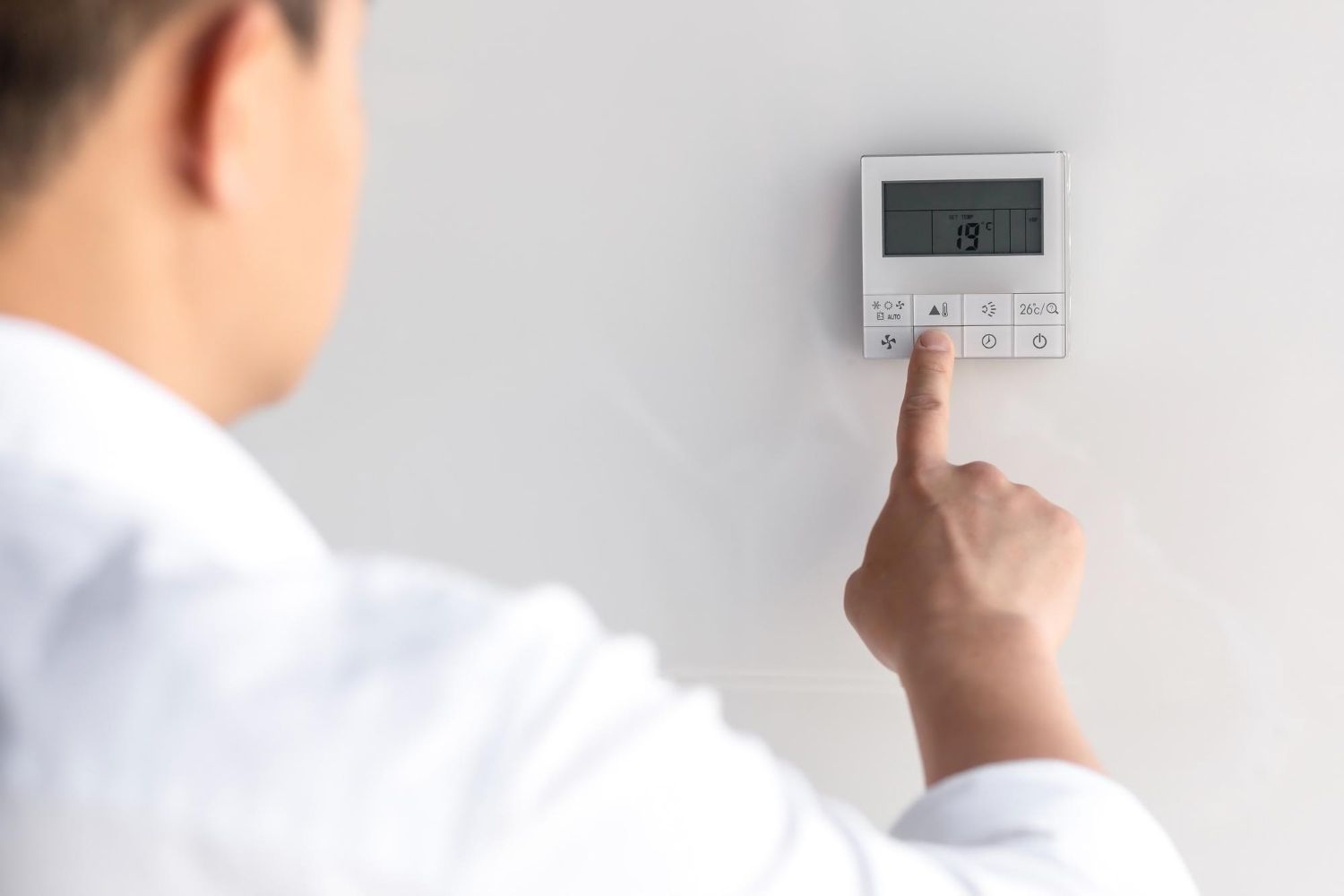 A man is pressing a button on a thermostat.