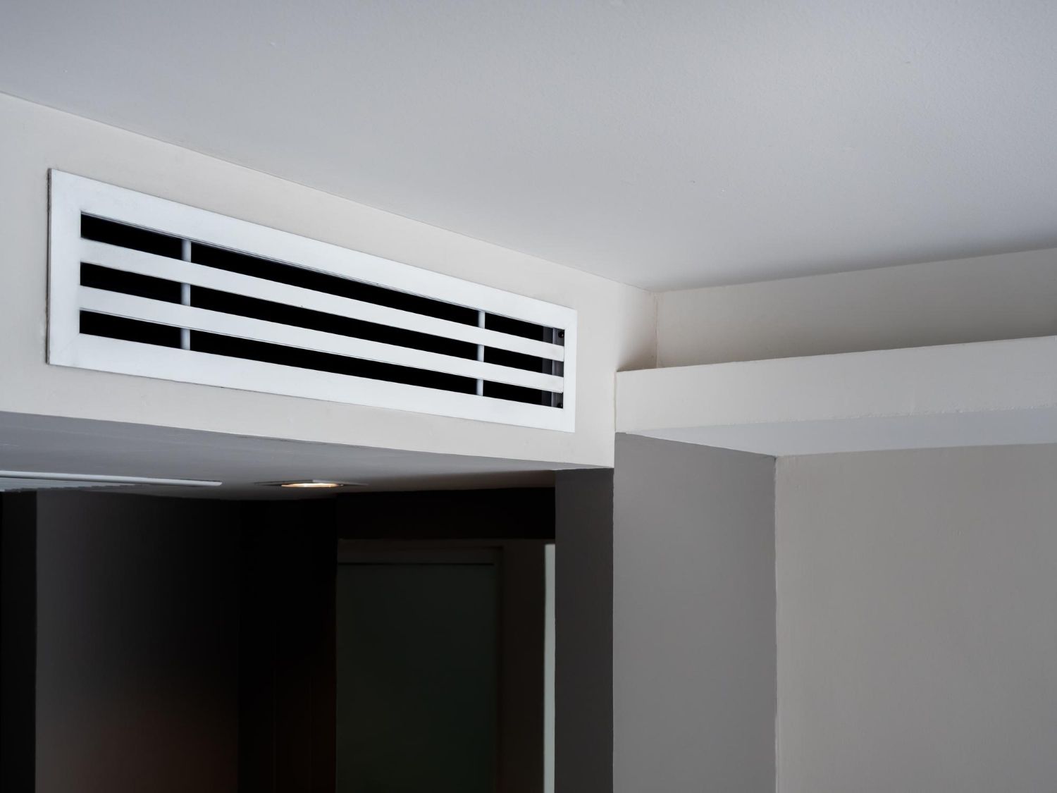 A white air vent is hanging from the ceiling of a room.