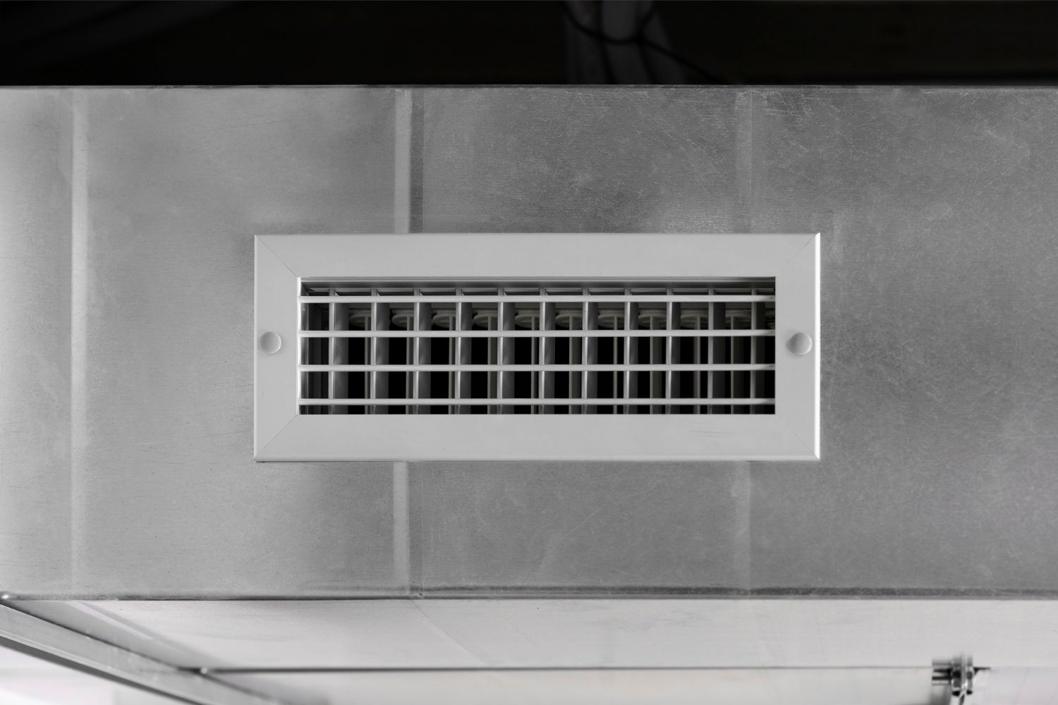 A white air vent is hanging from the ceiling of a room.