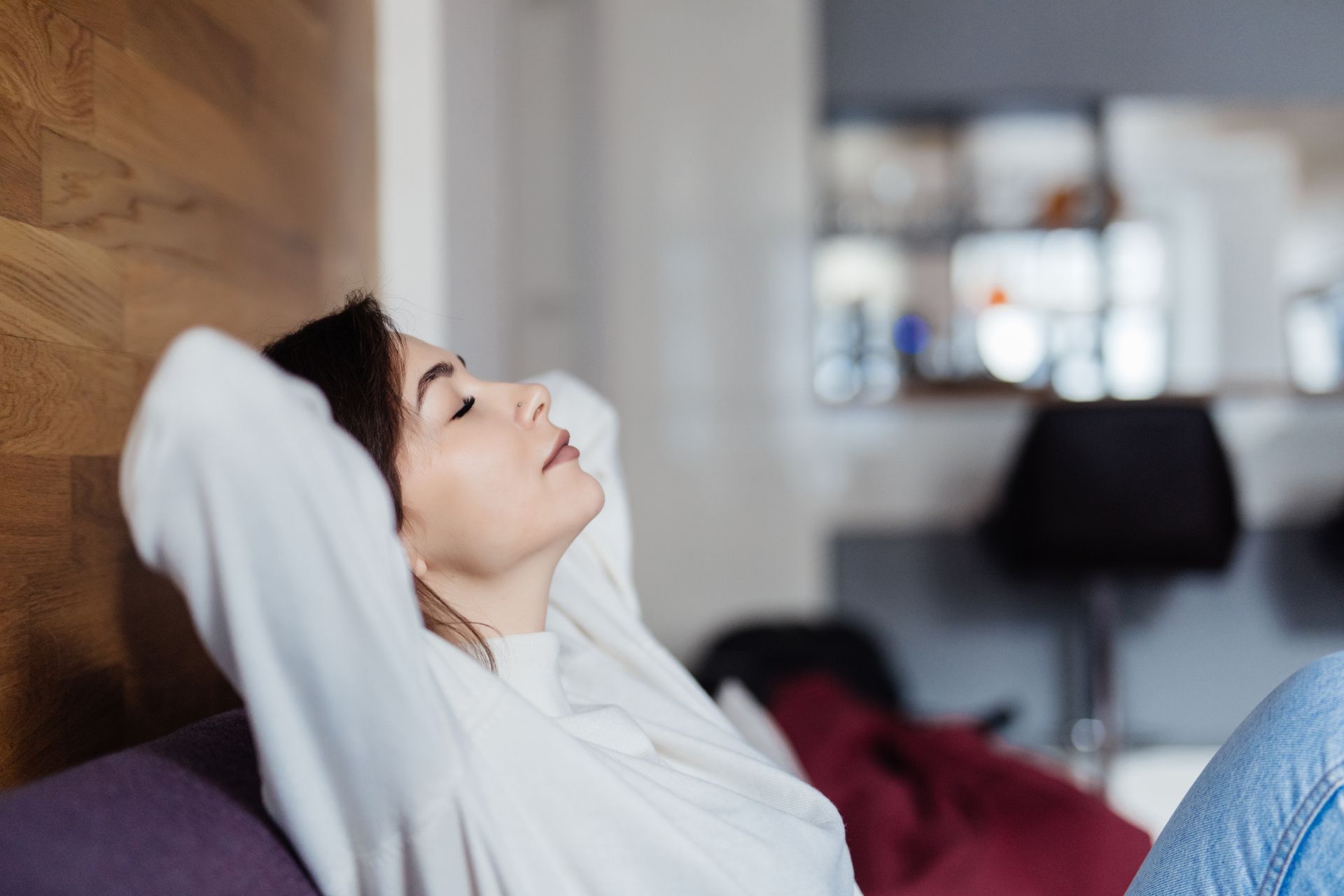 Woman relaxing with her hands behind her head on a sofa, eyes closed.