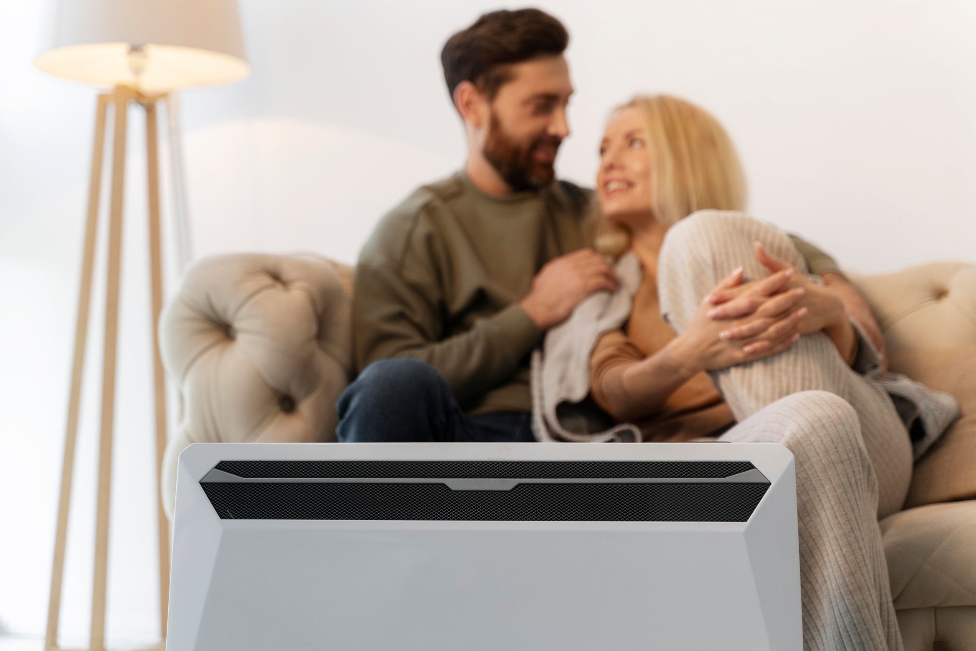 A man and a woman are sitting on a couch next to a heater.