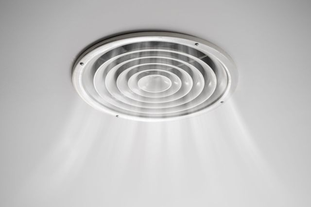 A round air vent on the ceiling with a light coming out of it.
