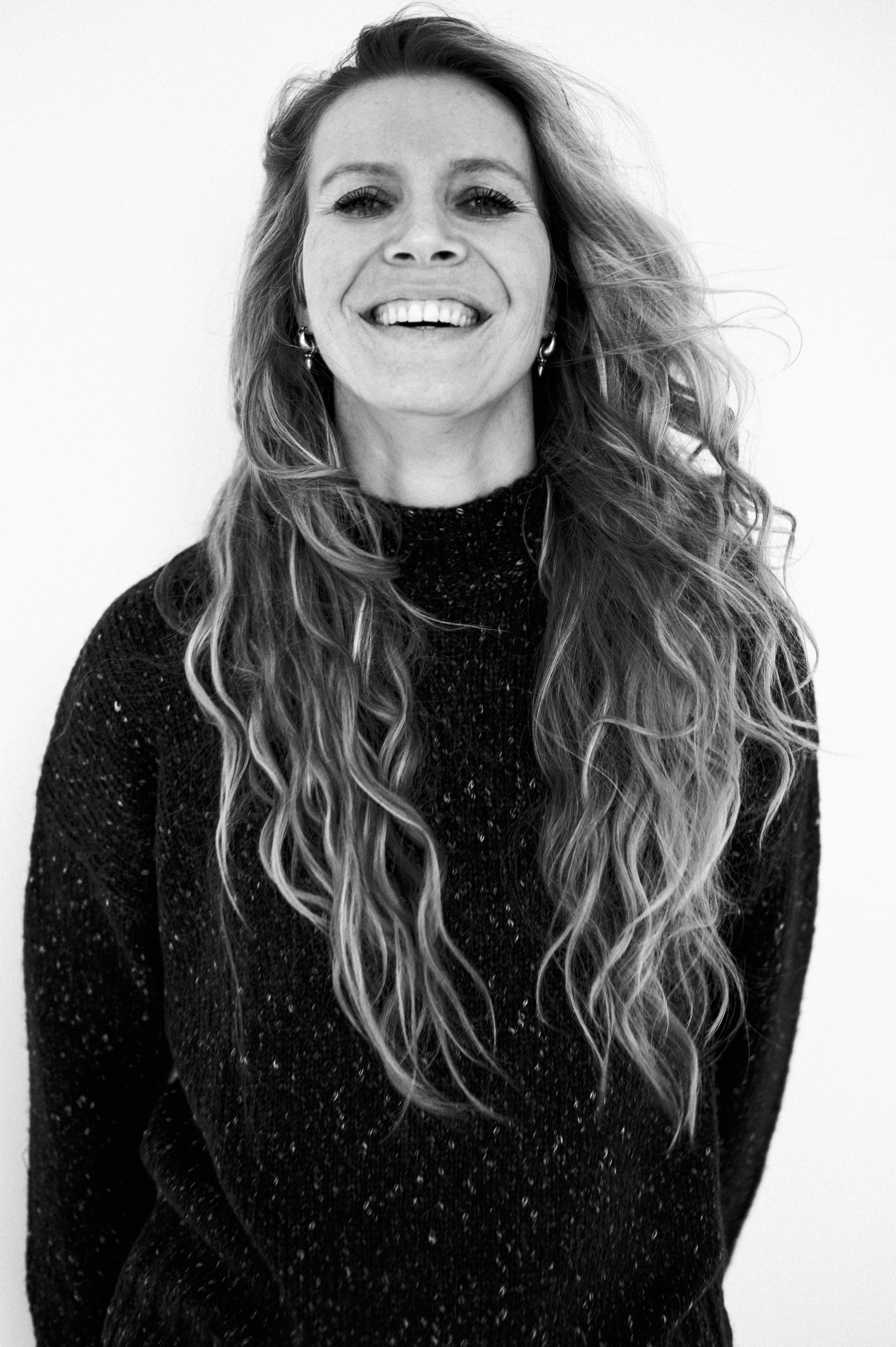 Debbie lacht breed, gekleed in een donkere trui, tegen een witte achtergrond.