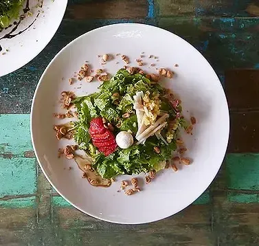 Un plato blanco cubierto con ensalada sobre una mesa de madera.