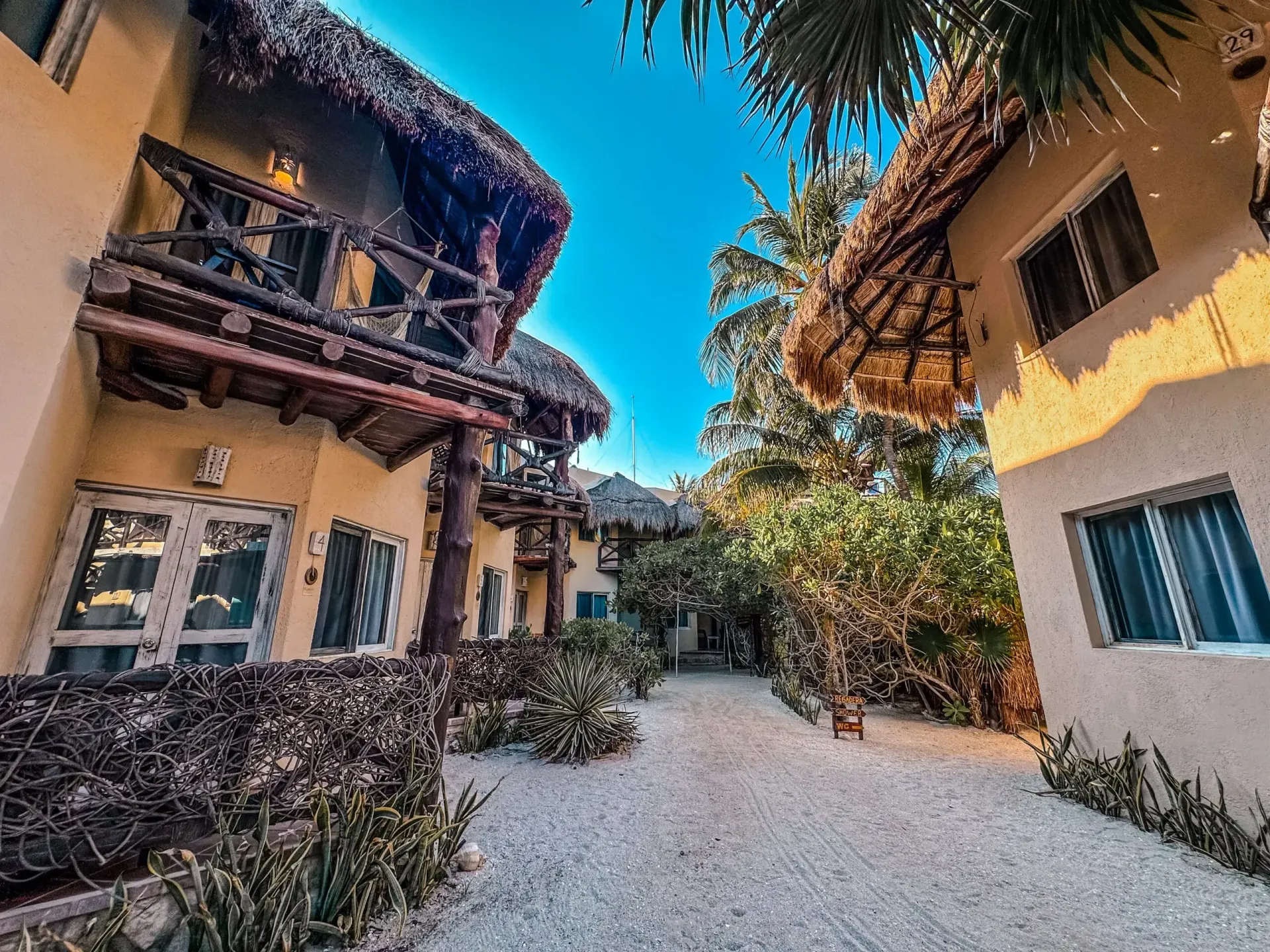 Edificios con techos de paja y balcones de madera, a lo largo de un camino de grava, bajo un cielo azul.