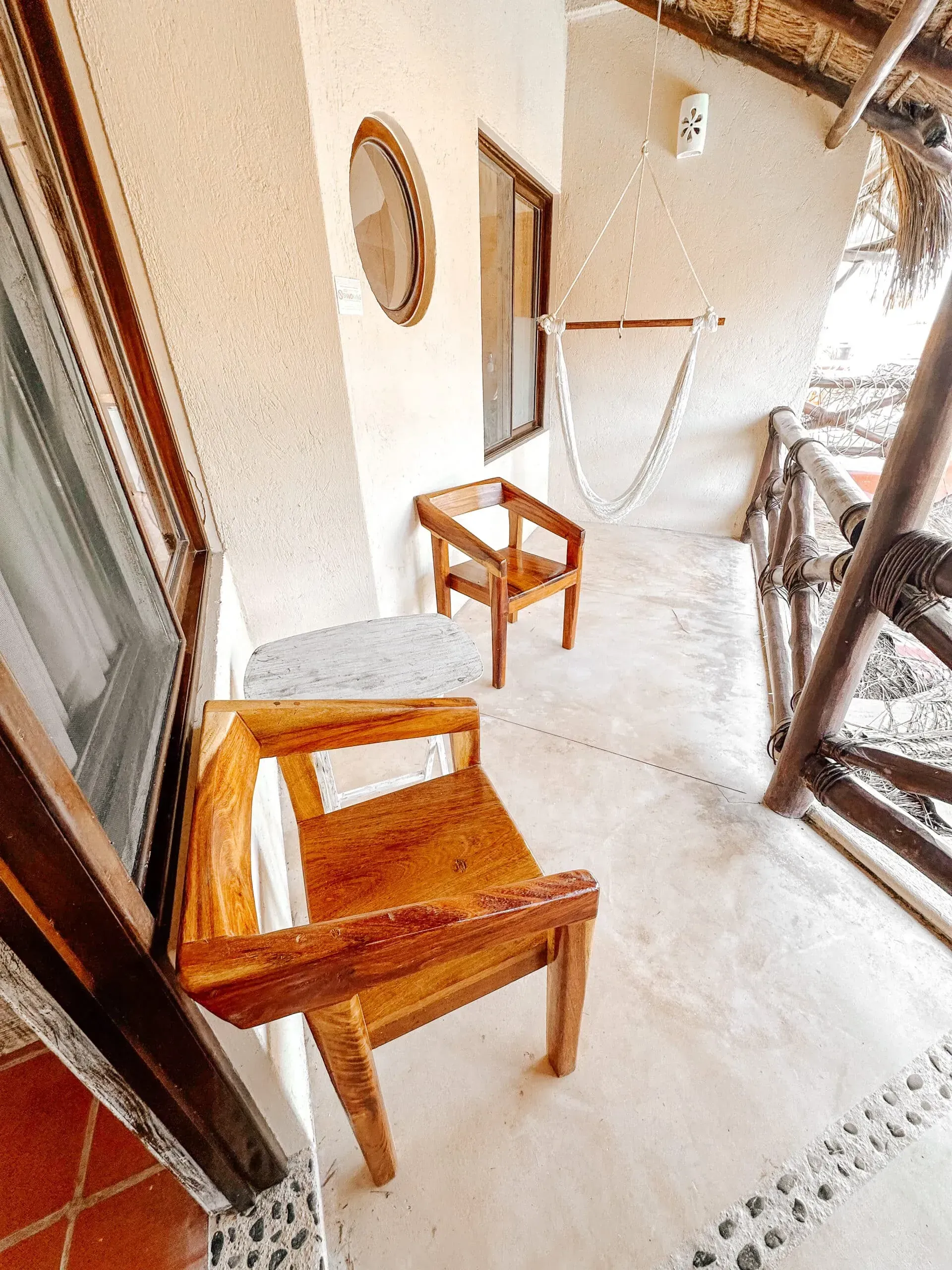 Sillas de madera en un balcón con pared de estuco blanco y techo de paja.