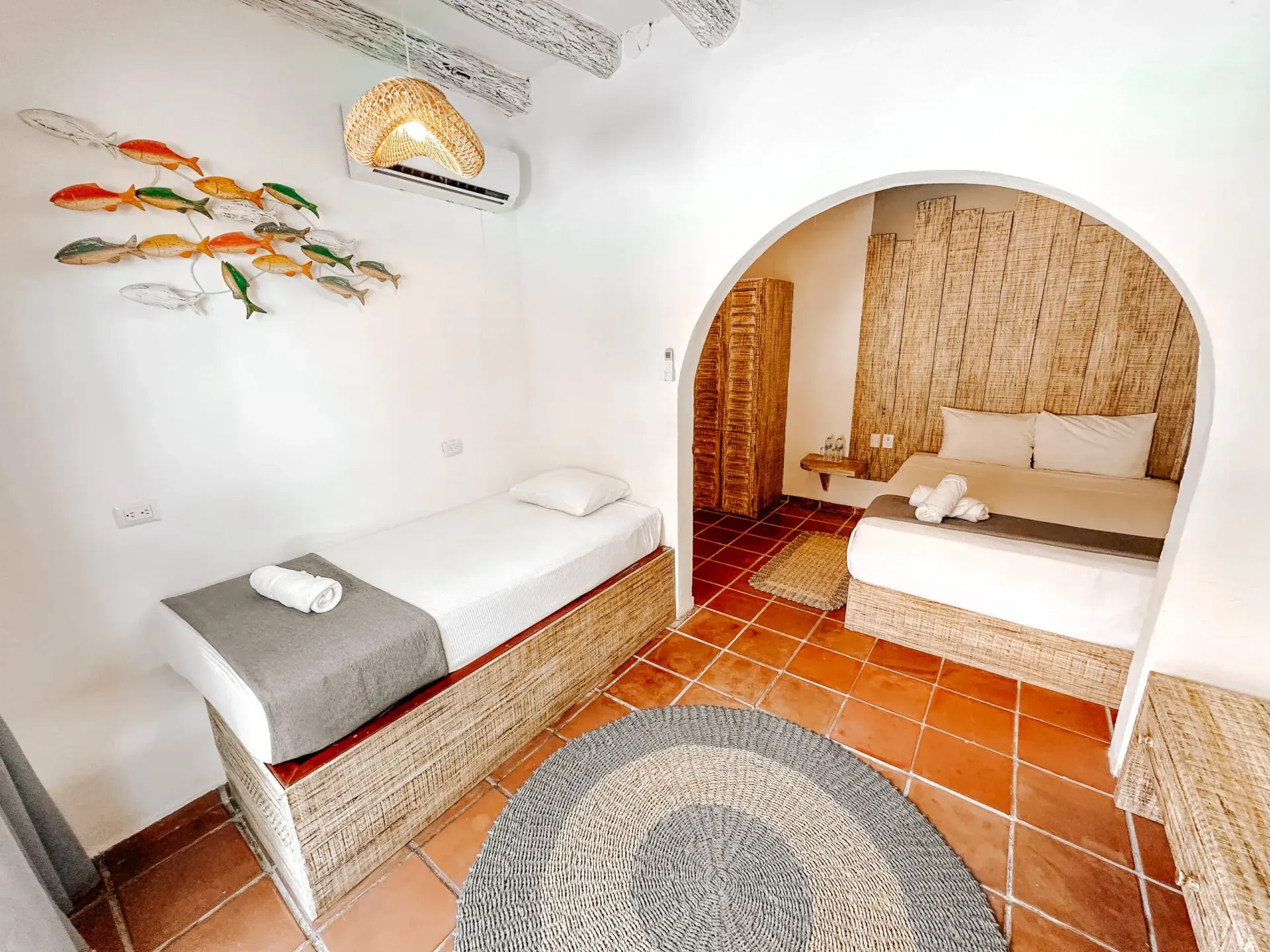 Dormitorio con una cama individual y una cama de matrimonio visible a través de un arco, tonos cálidos, arte de peces.