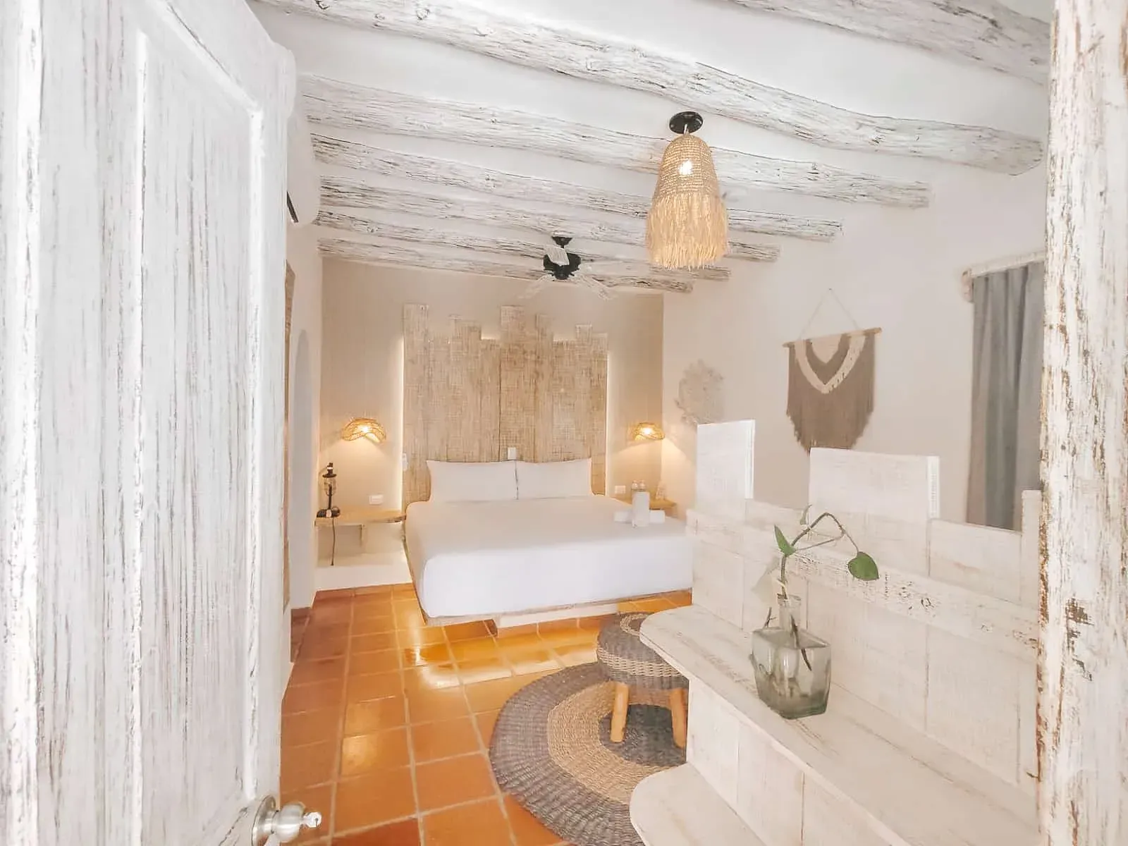 Interior del dormitorio, paredes blancas, vigas a la vista, decoración neutra, cama con sábanas blancas, luz natural.