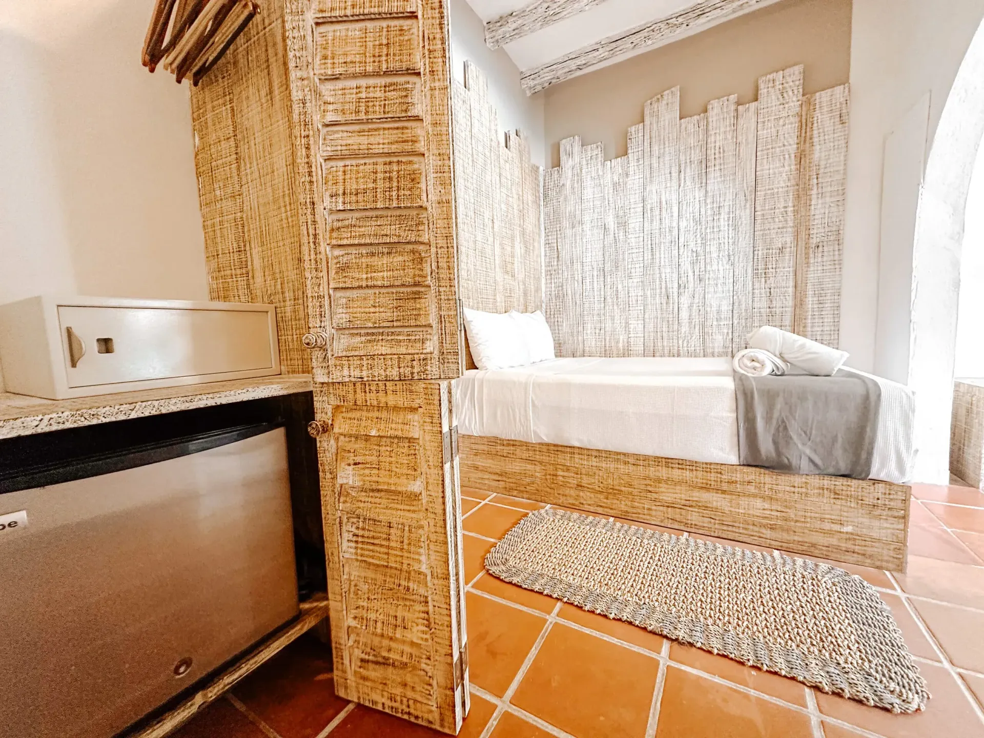 Dormitorio con paredes de madera texturizada, una cama y una alfombra sobre un piso de baldosas de terracota.