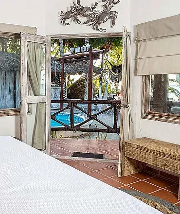 La puerta del dormitorio se abre a un balcón con vistas a una piscina y un entorno tropical.